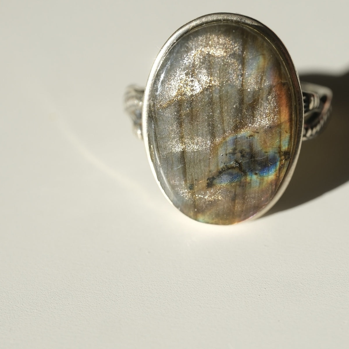 Centred oval Labradorite ring showing multicoloured flash and ornate band