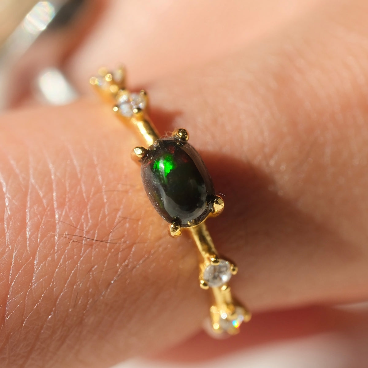 Ethiopian Black Opal adjustable ring with a gold-coloured band and clear accents, shown on a finger