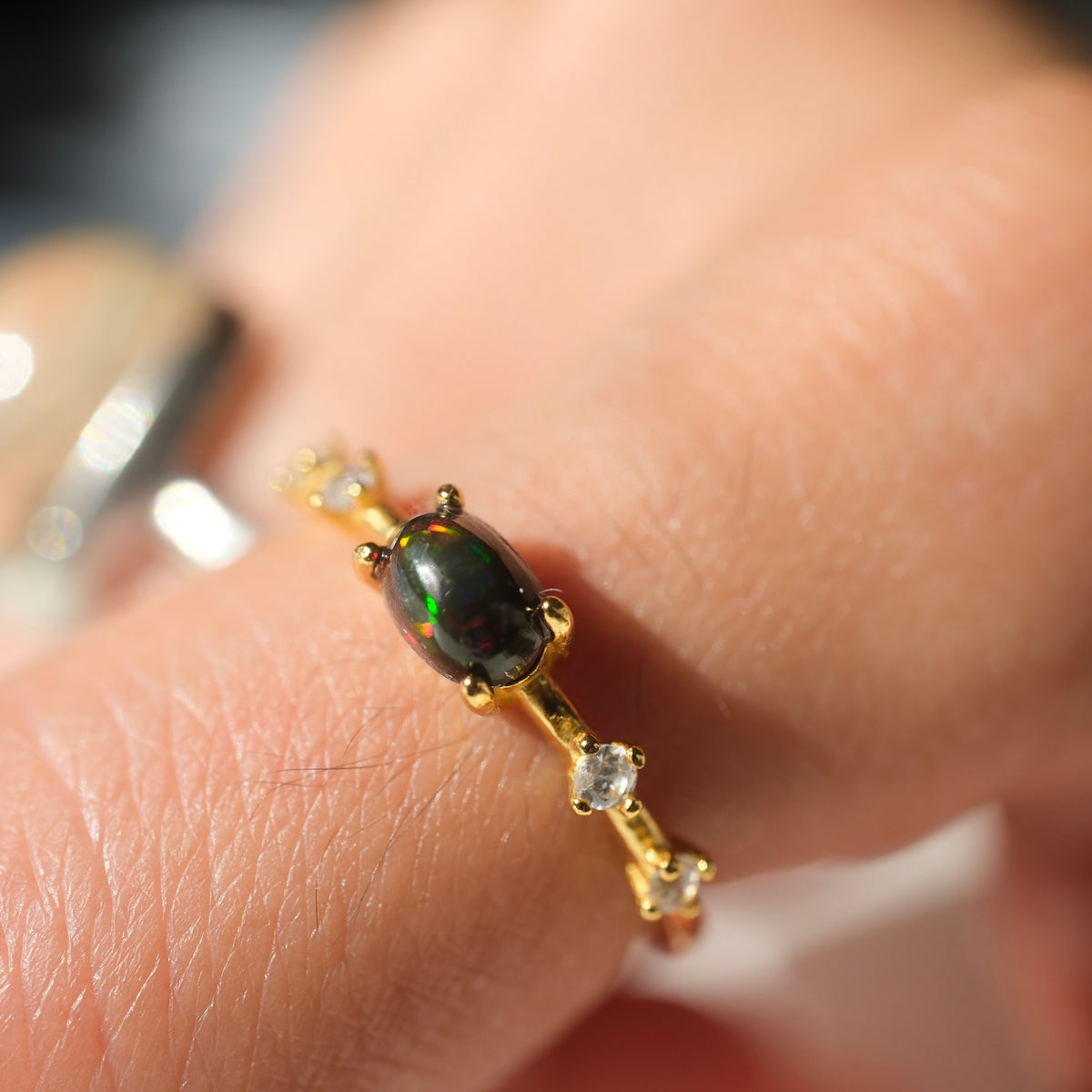 Ethiopian Black Opal adjustable ring with a gold-coloured band and clear accents, shown on a finger