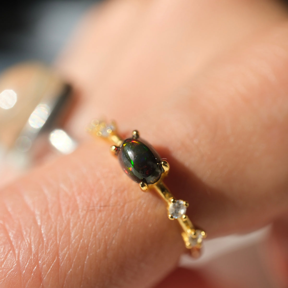 Ethiopian Black Opal adjustable ring with a gold-coloured band and clear accents, shown on a finger