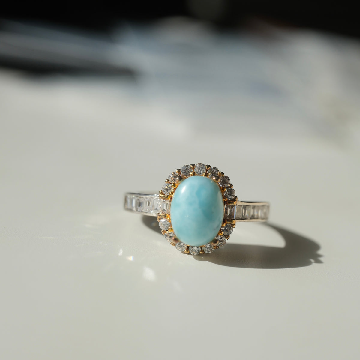 Larimar S925 adjustable ring with an oval blue stone, clear halo, gold-coloured setting details and rectangular clear shoulder accents