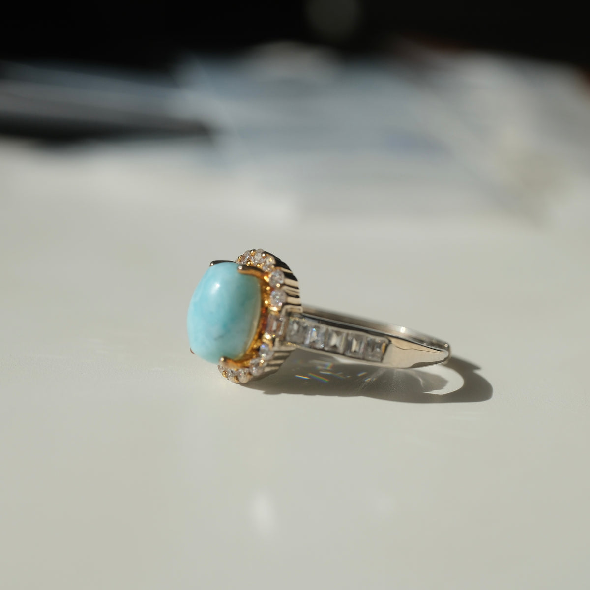 Larimar S925 adjustable ring with an oval blue stone, clear halo, gold-coloured setting details and rectangular clear shoulder accents