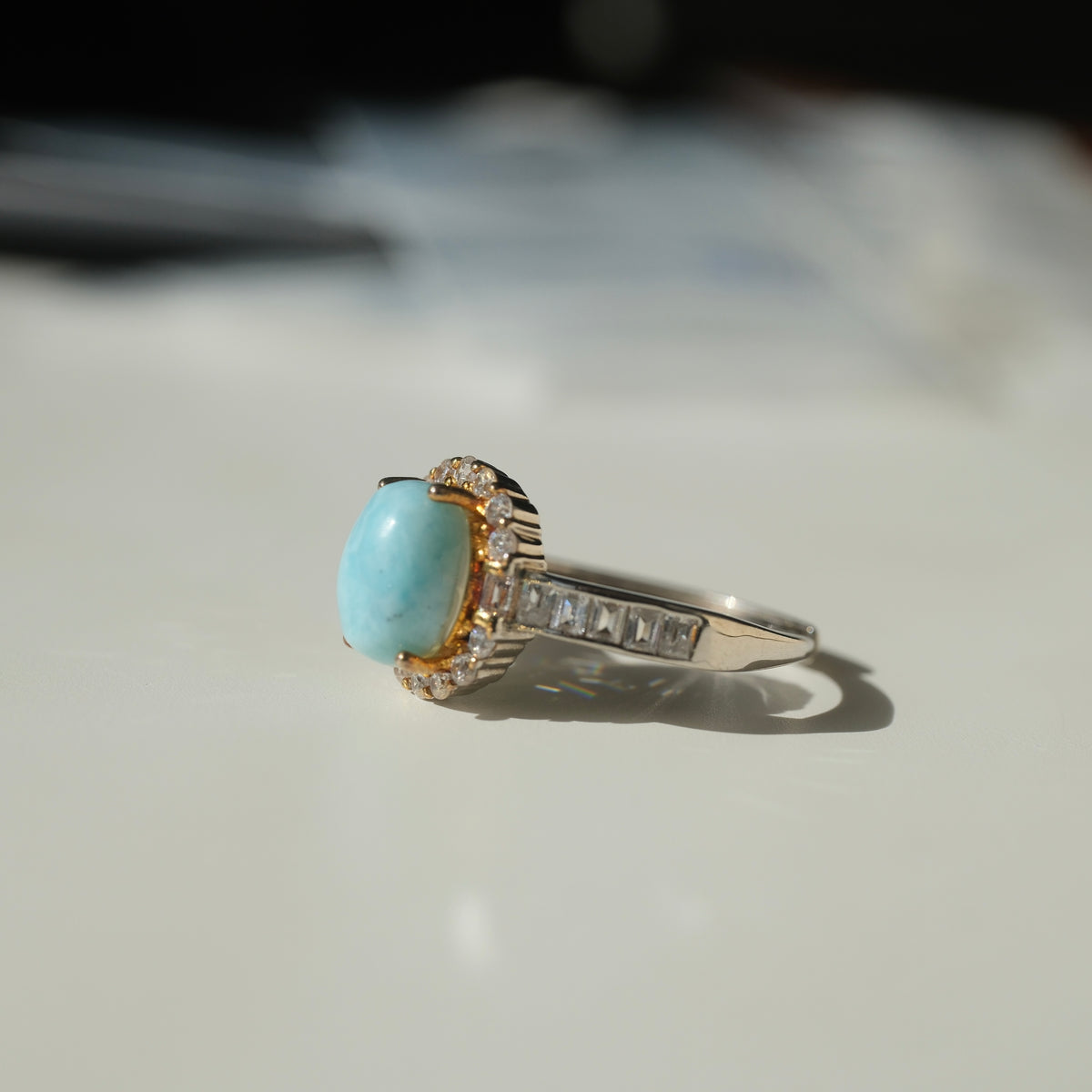 Larimar S925 adjustable ring with an oval blue stone, clear halo, gold-coloured setting details and rectangular clear shoulder accents