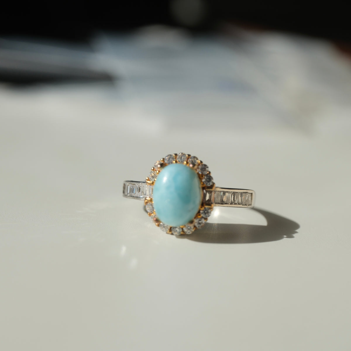 Larimar S925 adjustable ring with an oval blue stone, clear halo, gold-coloured setting details and rectangular clear shoulder accents