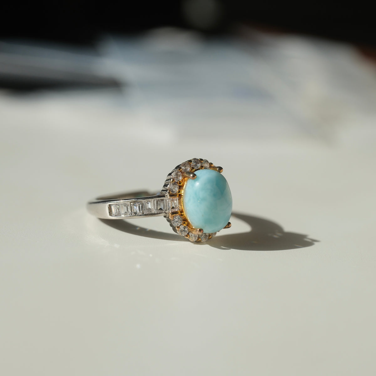 Larimar S925 adjustable ring with an oval blue stone, clear halo, gold-coloured setting details and rectangular clear shoulder accents