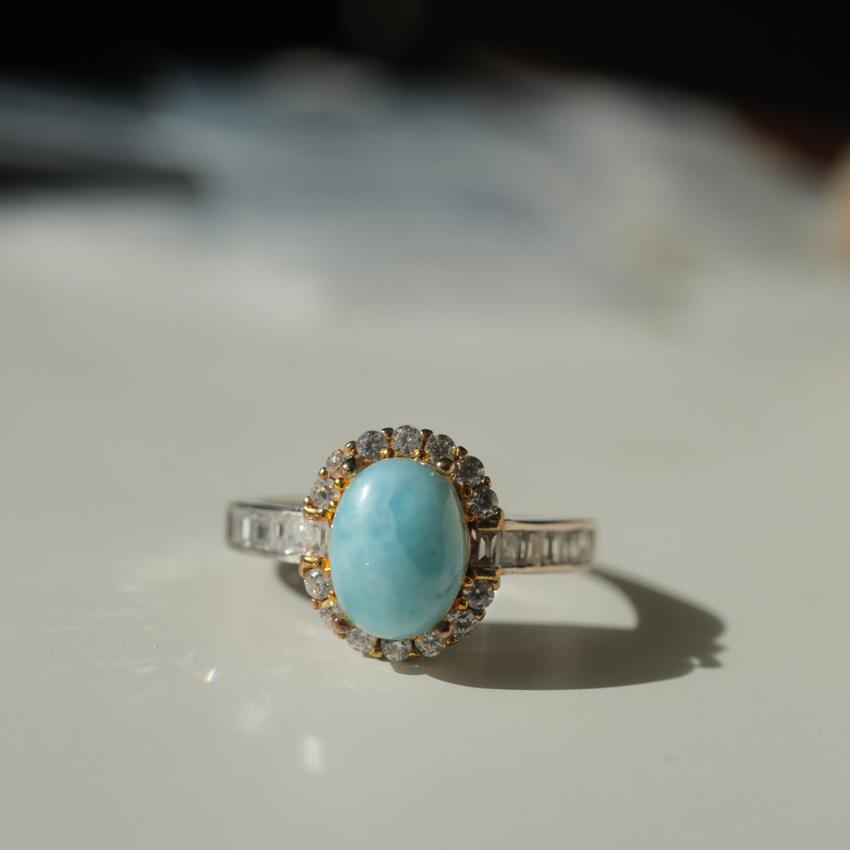 Larimar S925 adjustable ring with an oval blue stone, clear halo, gold-coloured setting details and rectangular clear shoulder accents