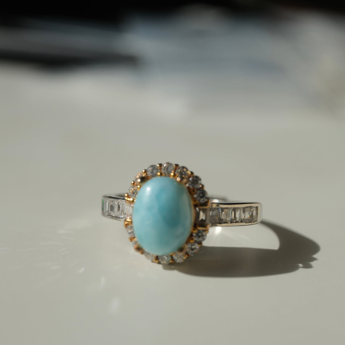 Larimar S925 adjustable ring with an oval blue stone, clear halo, gold-coloured setting details and rectangular clear shoulder accents